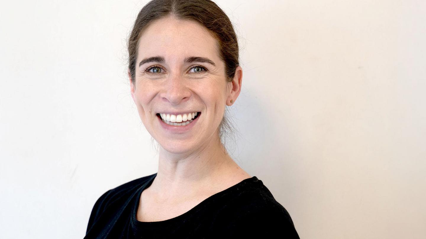 Woman with dark hair and wearing a black top smiles broadly at the camera