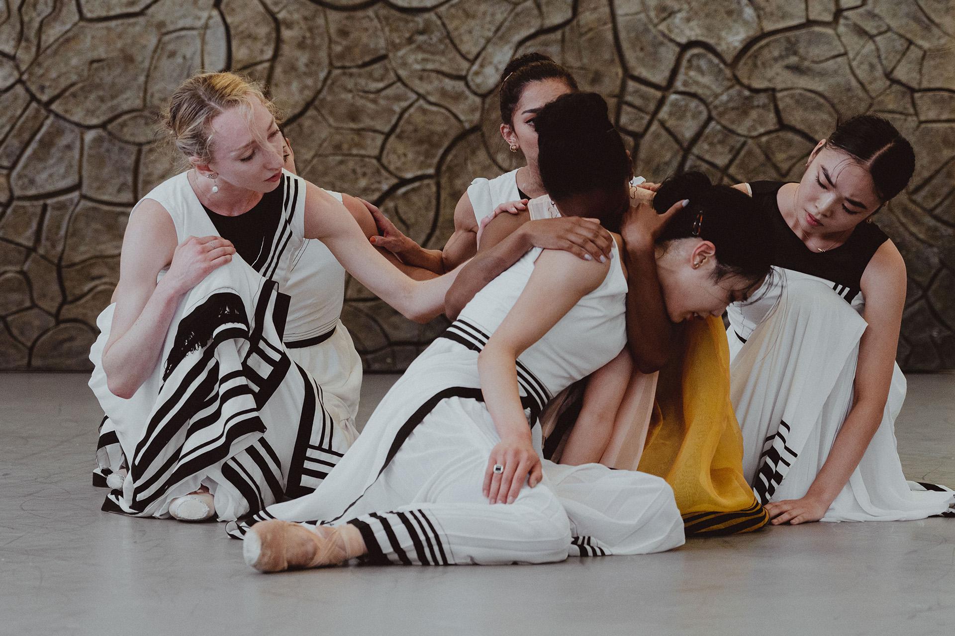 One dancer embraces another for comfort while others reach out in support