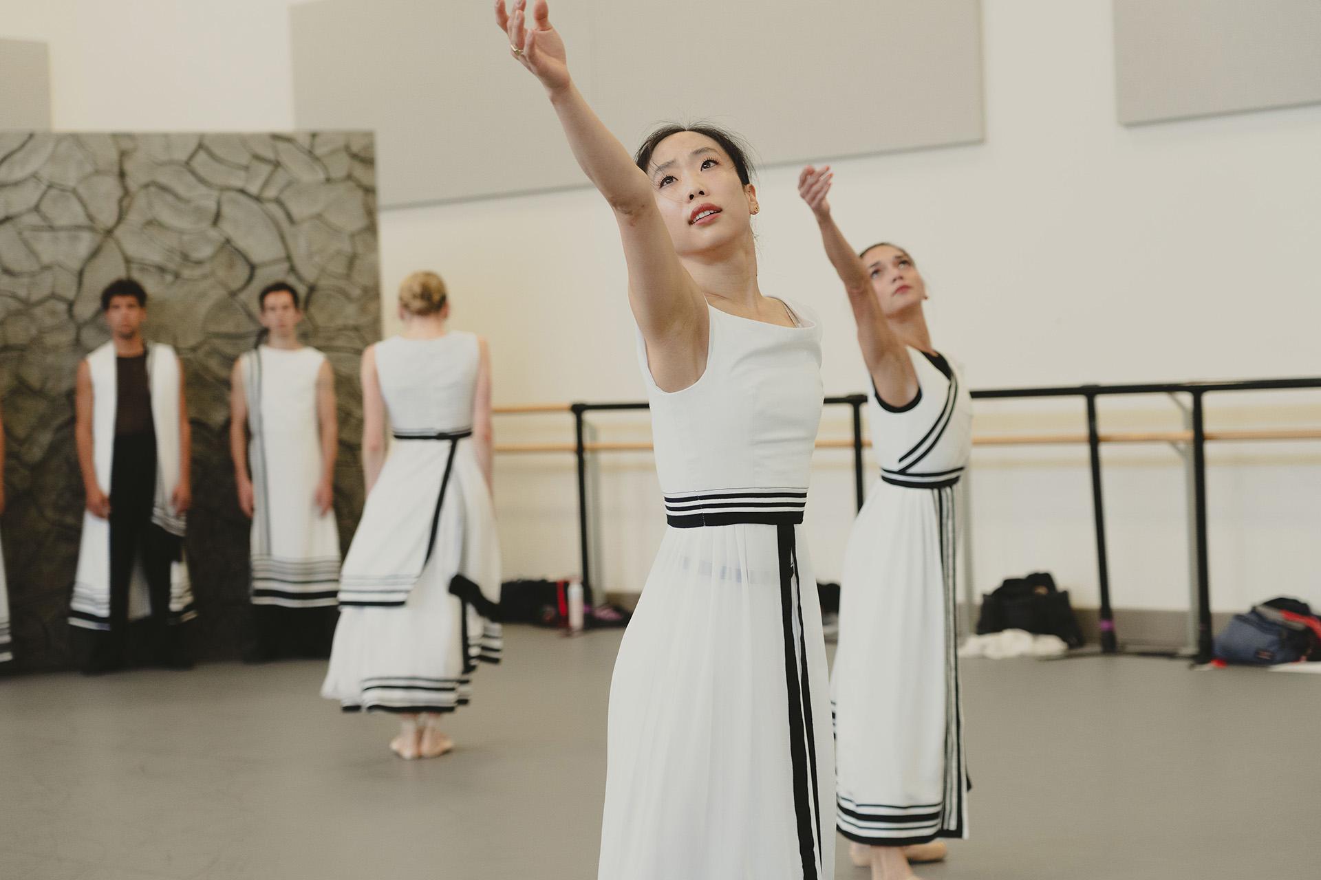 Dancers stands one arm raised and following that line with their gaze.