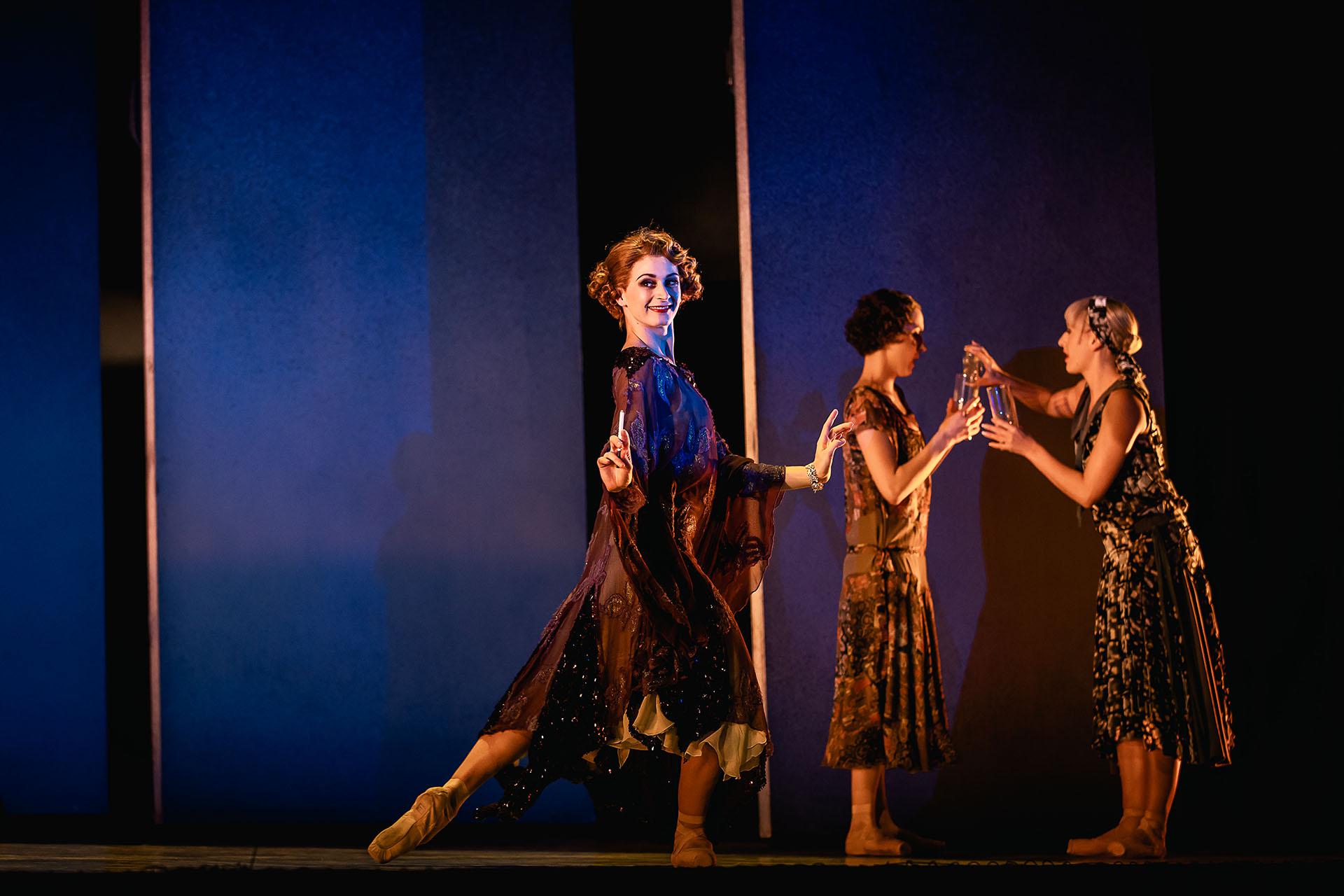 Dancer in a burgundy 20s-style dress stands with her hands in a classic flapper pose