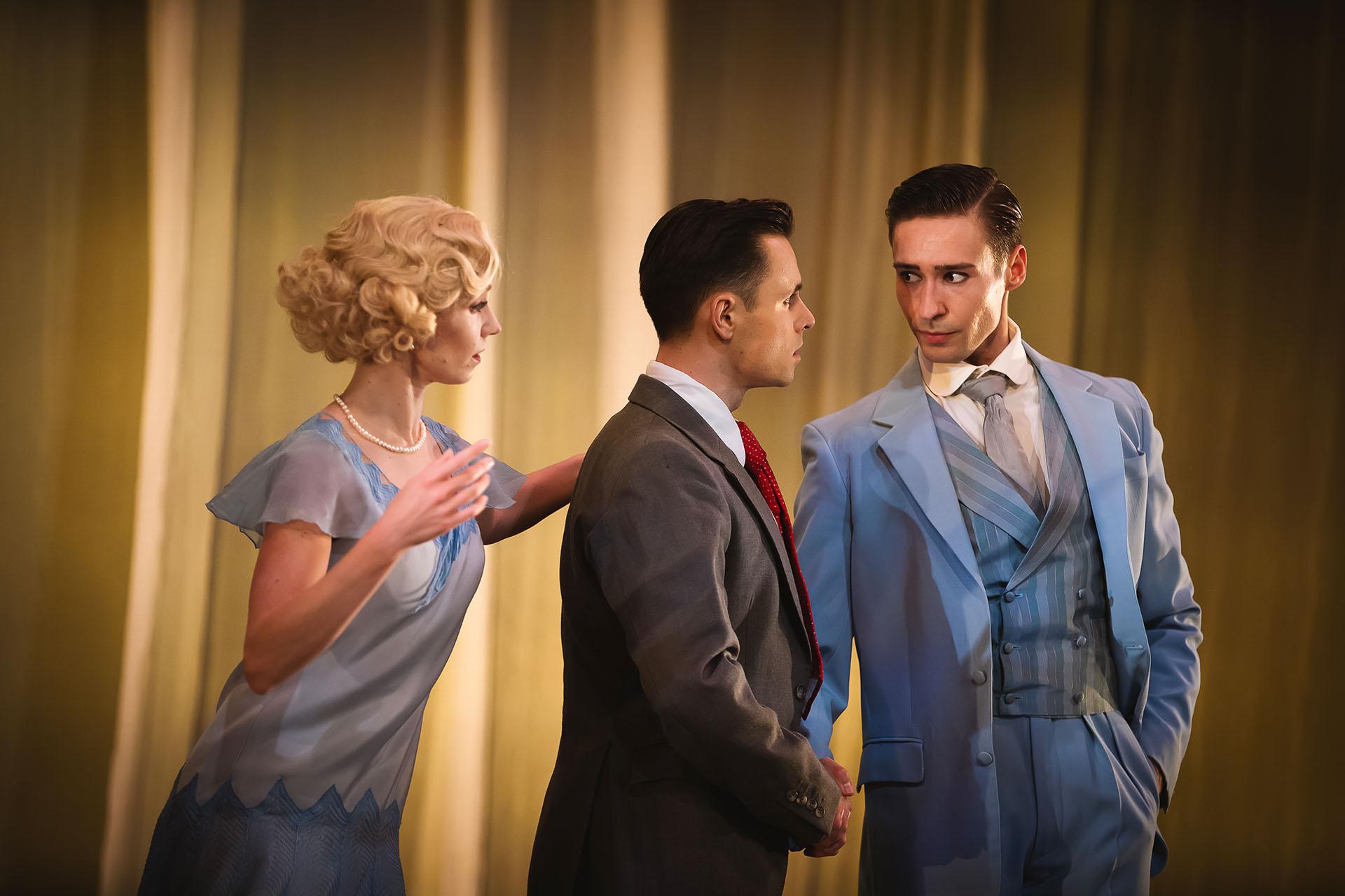 A wife looks over her husband's shoulder at her lover as he shakes hands with the husband