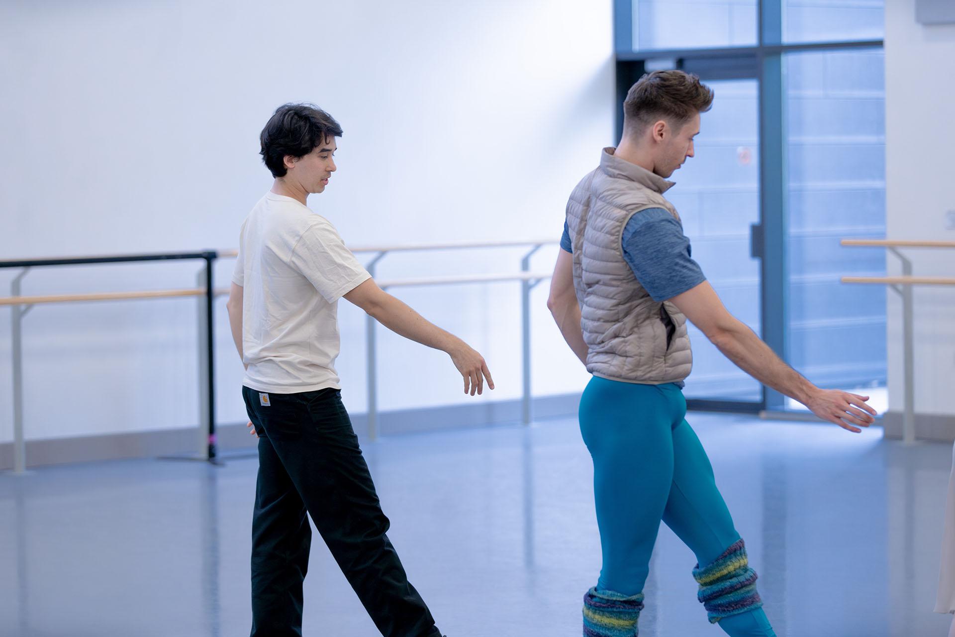 A choreographer to the left mirrors a dancers position, one arm and one leg in front.