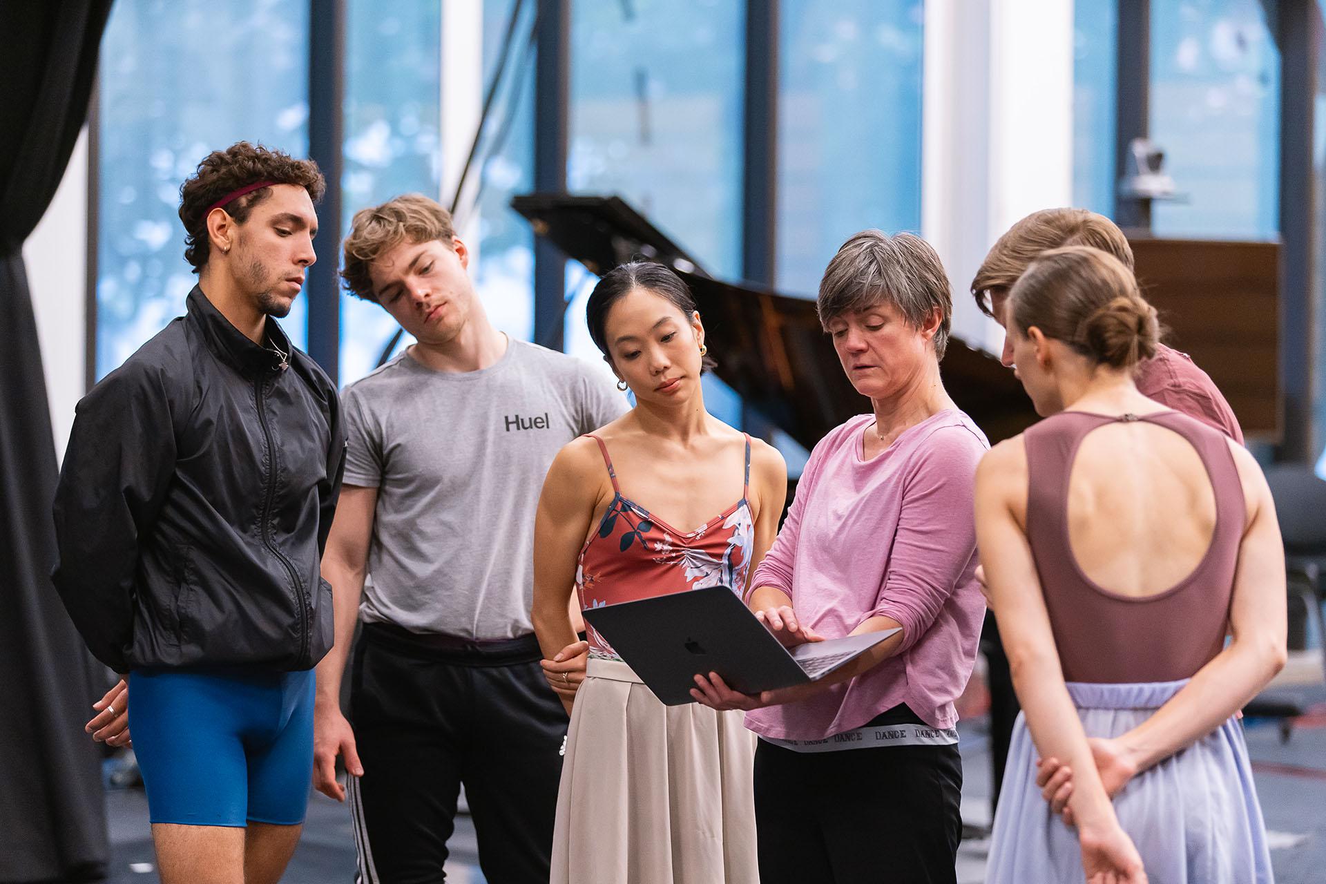 Dancers look on to Christelle's laptop, watching a previous cast perform the roles they are rehearsing for