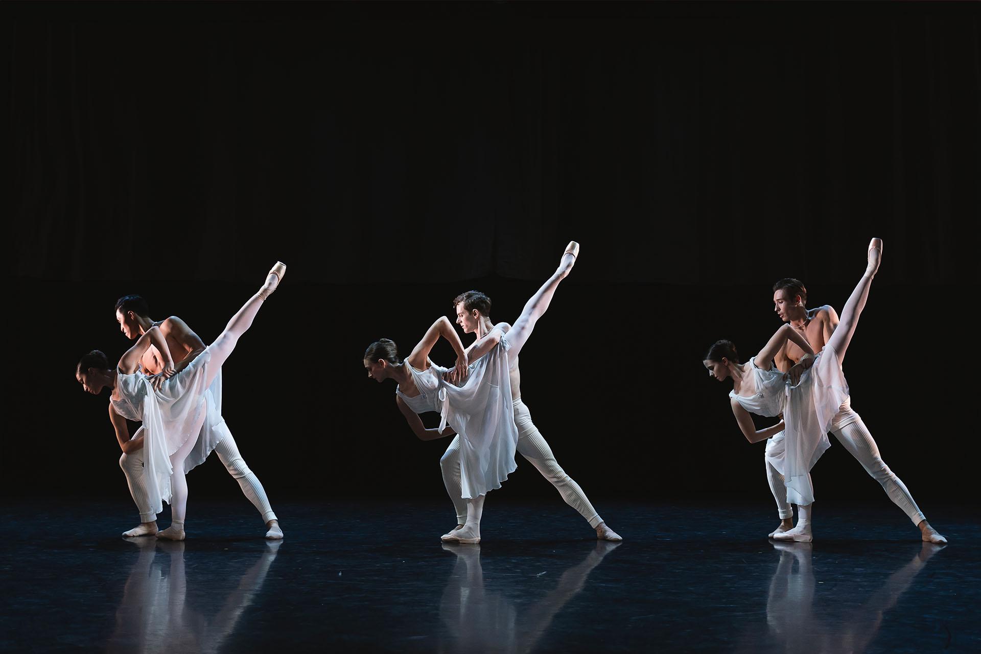Three couples, each wearing white, a male holds steady a female who is leaning forward on one foot while the other leg is extended in the air behind her