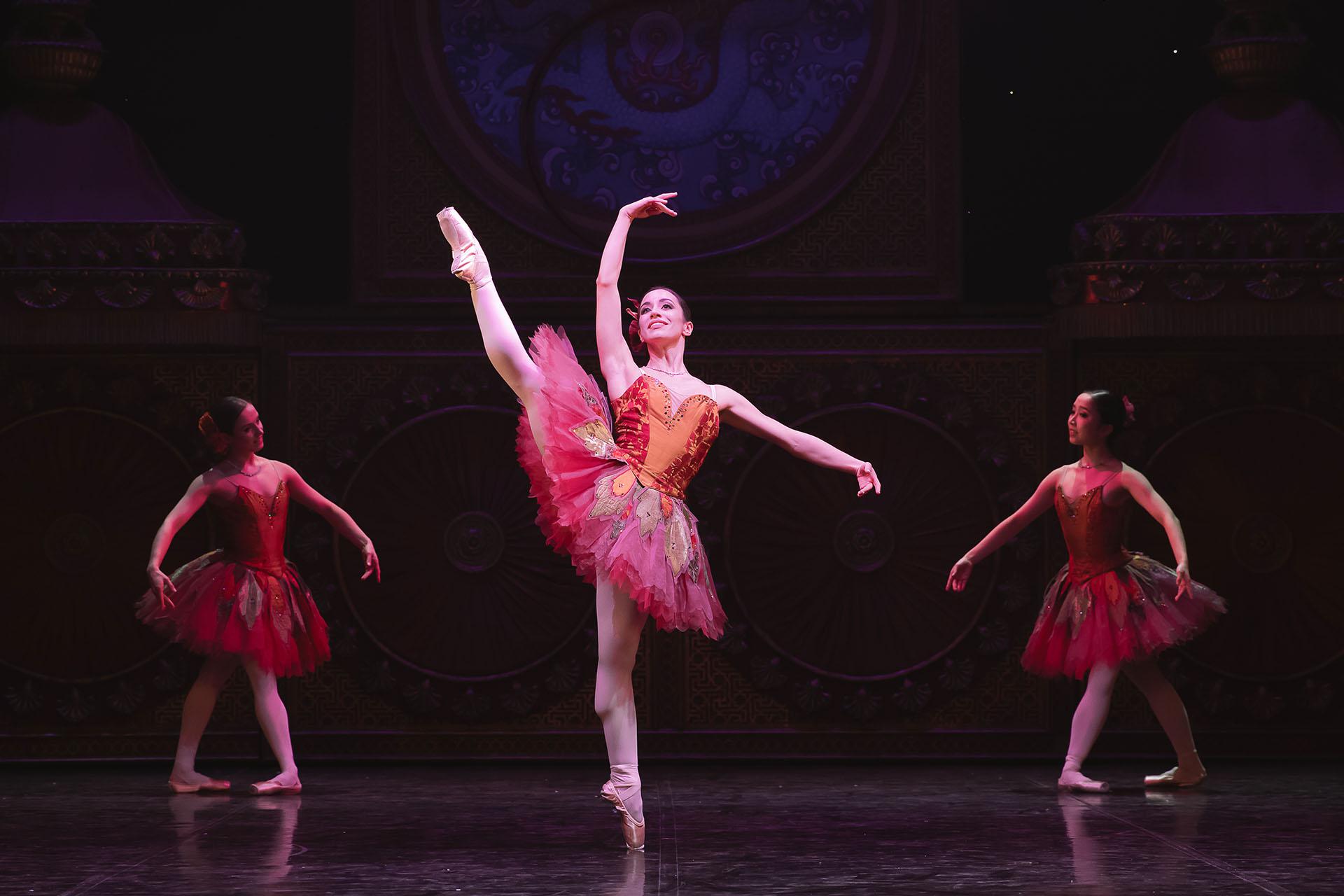 Woman in a pink tutu standing en pointe on one foot and her other leg is raised above her head