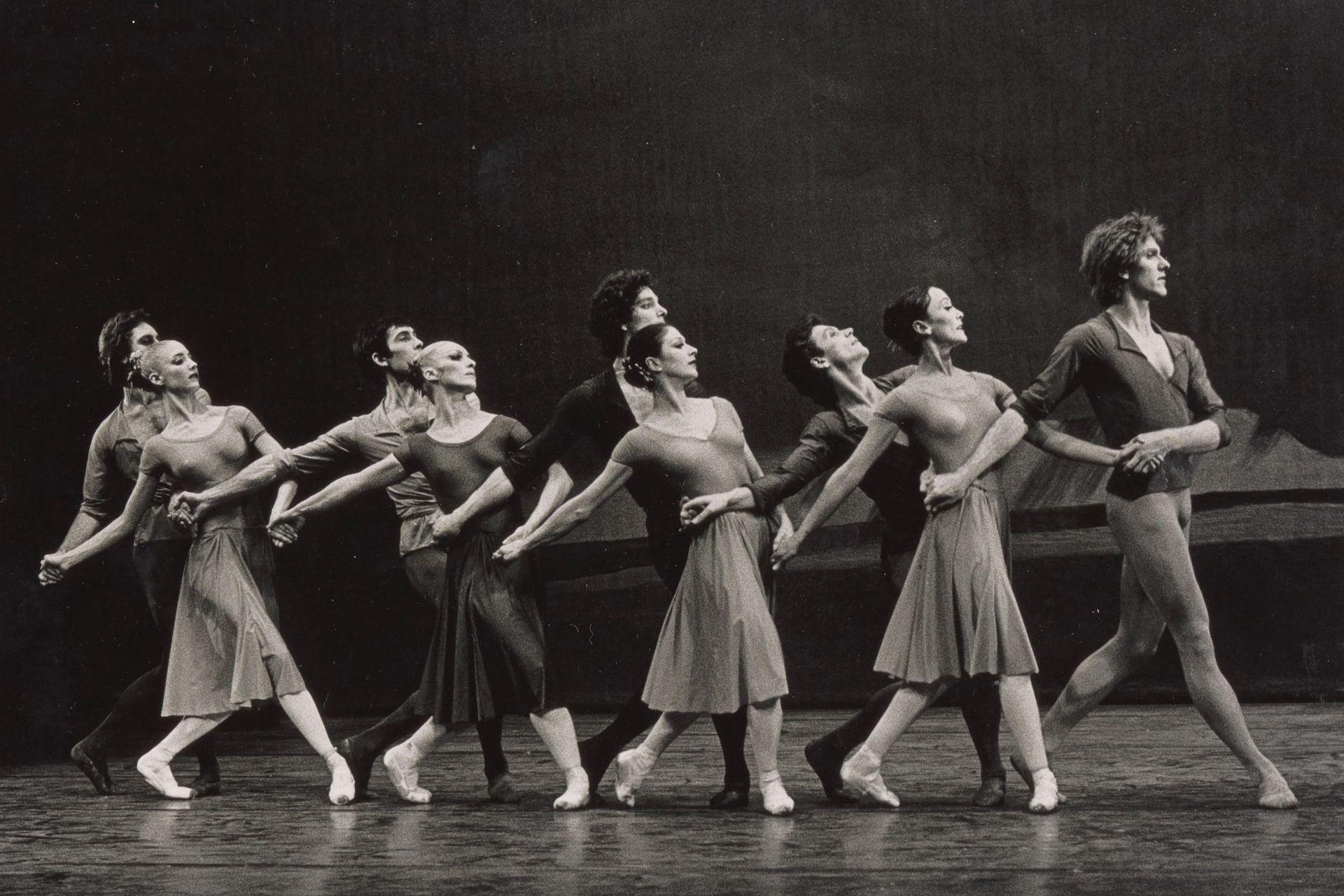 A black and white photo of Dutch National Ballet dancers in the 1970s performing Four Last Songs. They stand in a line across the stage, holding hands and interlocking arms, looking to the right.