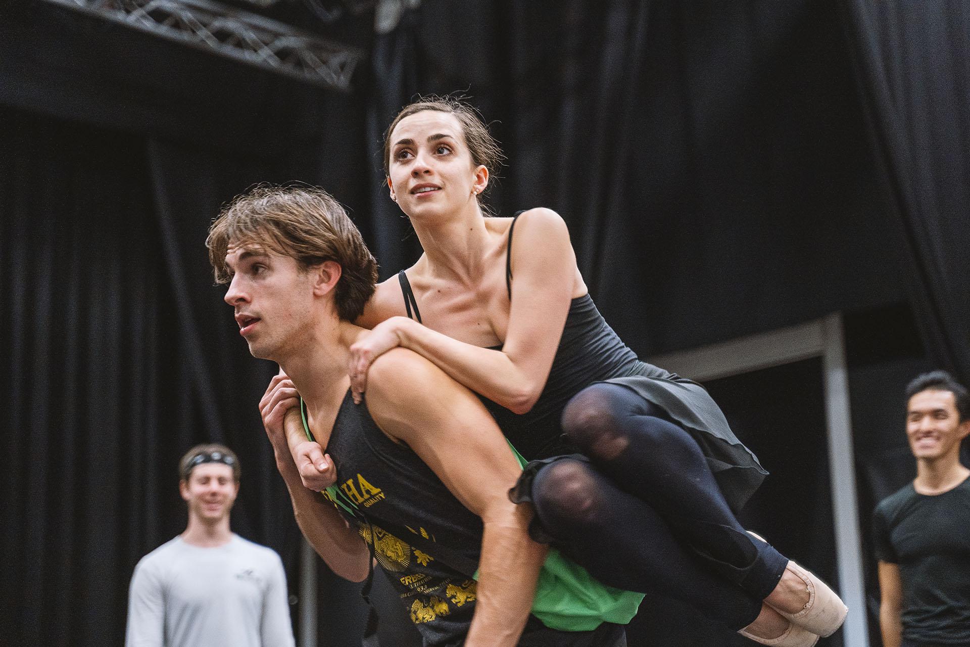 A dancer being carried on the back of another, both with determined looks