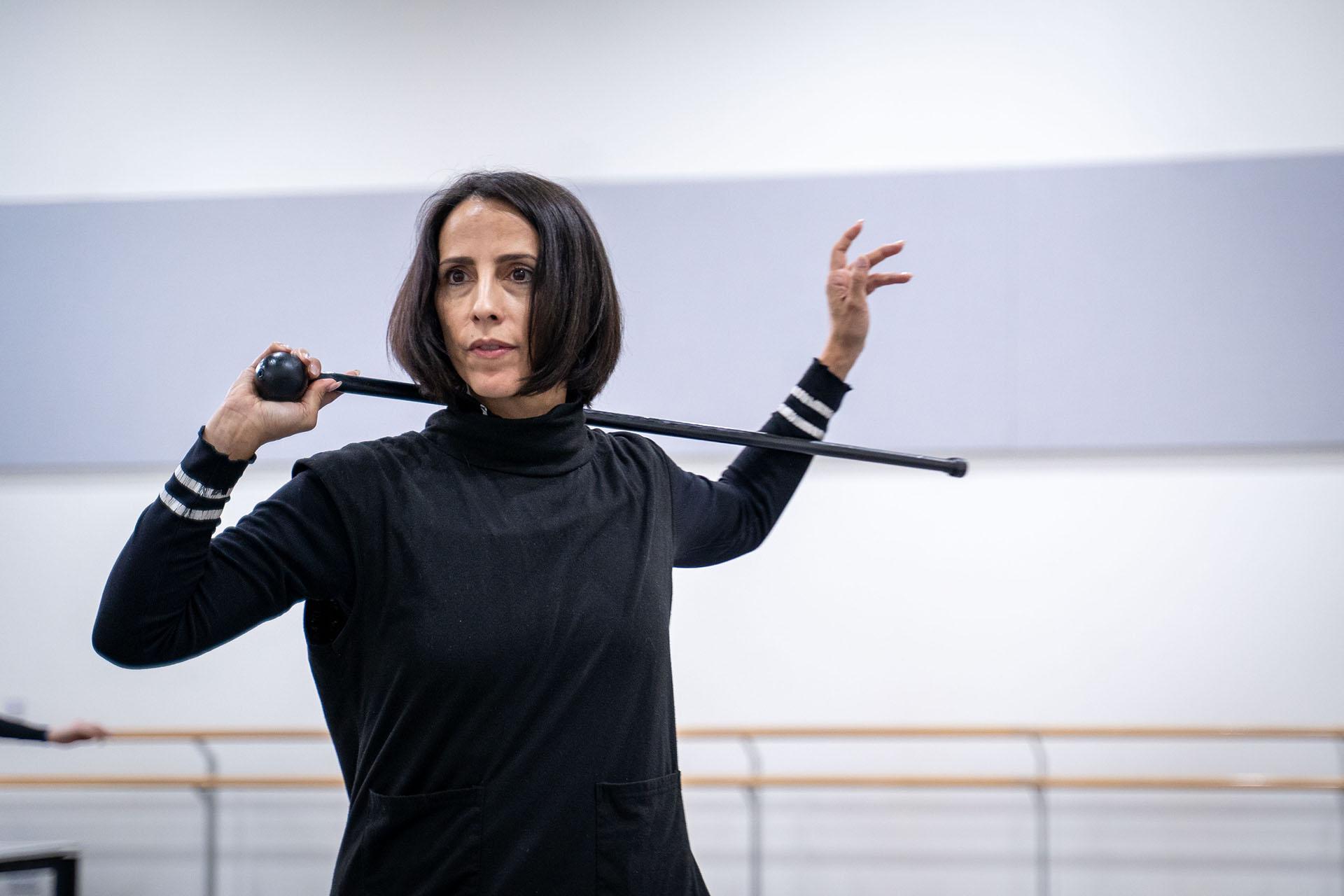 Woman with dark hair holds riding crop behind her neck