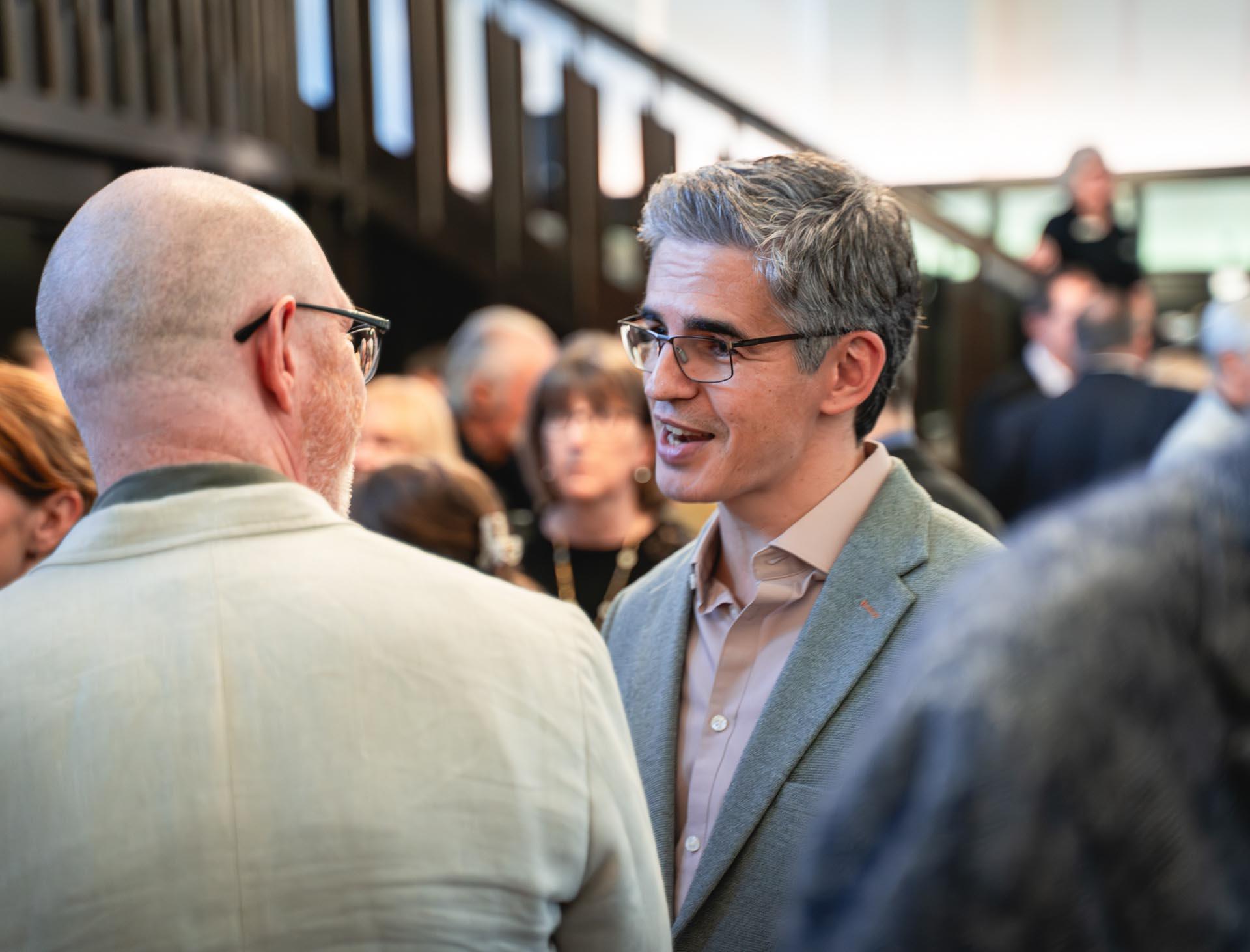 A man in a grey suit talking to others at a reception