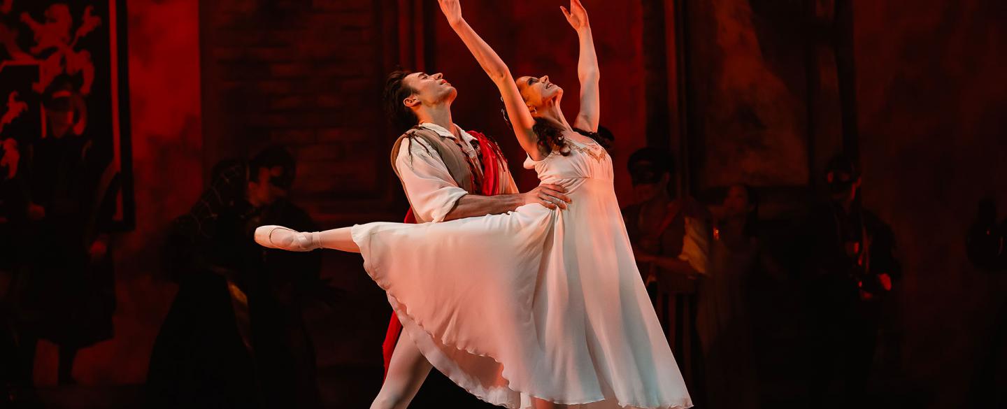 Juliet stands en pointe with her arms above her head, Romeo holds her by the waist