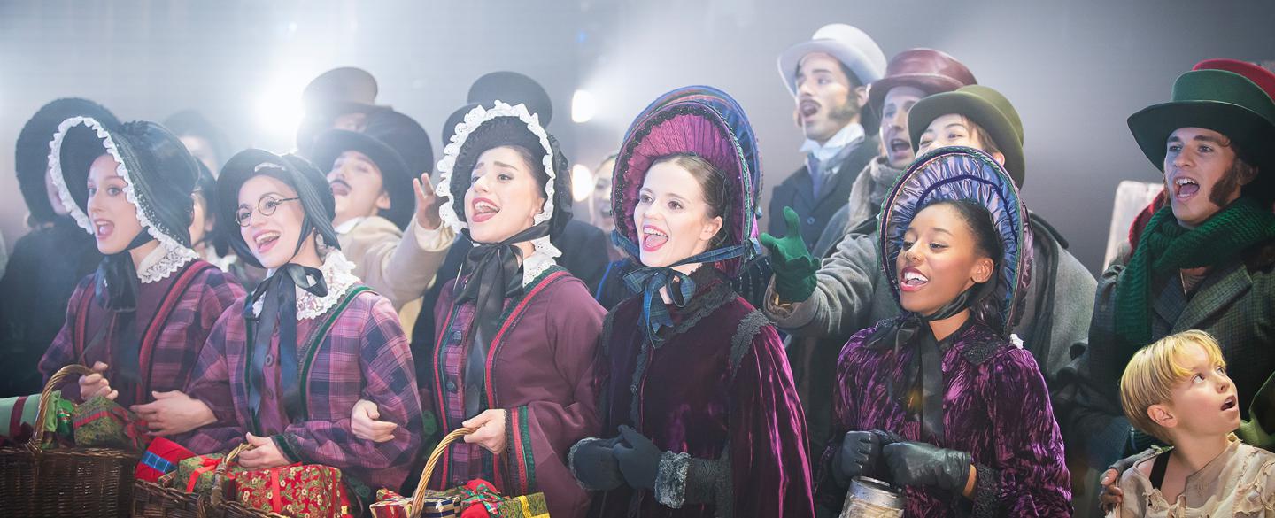 A close up photo of a group of dancers singing in Victorian era clothing
