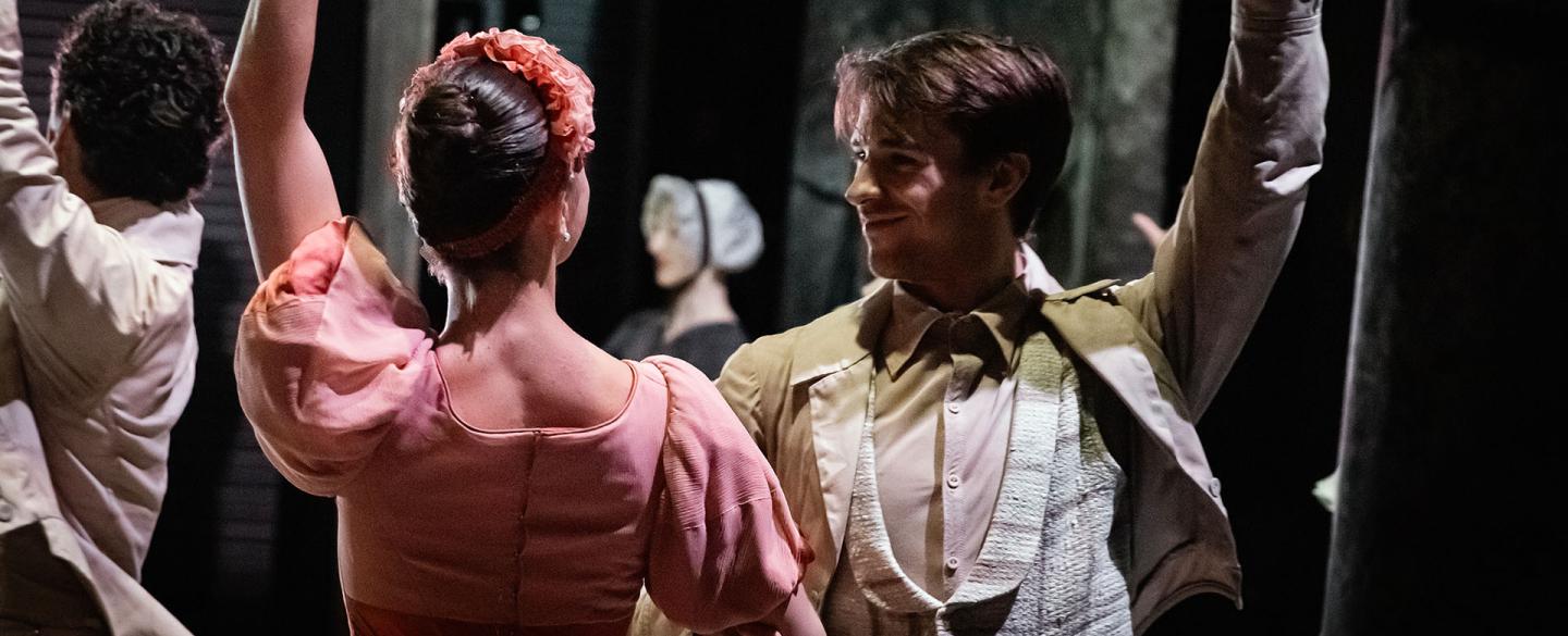 Two dancers facing each other, one arm clasping the others, their other arm raised behind them