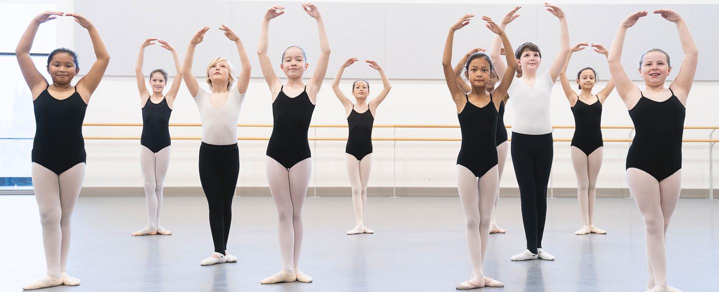 Students in a class, all with their hands above their heads, knees and ankles together