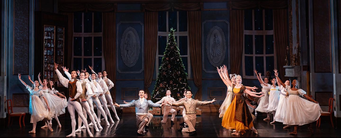 A party of dozens dressed in Regency attire all striking a pose, Christmas tree in the background