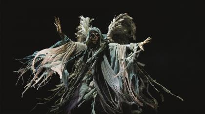 Against an inky black background, the skeletal and winged form of the Ghost of Christmas Yet to Come spreads his arms ominously