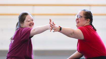 Two dancers in an Ability class sit across from each other on the floor, touching hands and smiling