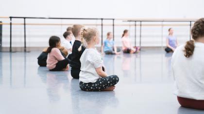 Children sat in a semi-circle cross legged on a dance floor