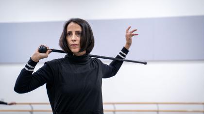 Woman with dark hair holds riding crop behind her neck